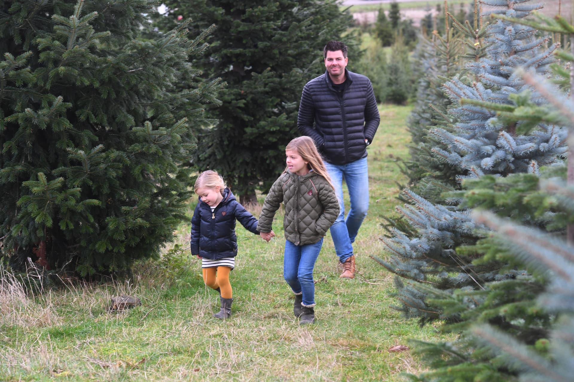 Vader met twee kinderen loopt tussen de kerstbomen
